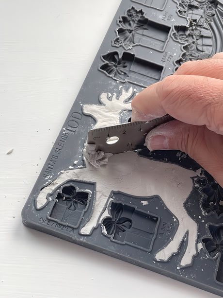Hand trimming plaster from I.O.D. Santa’s Sleigh Mould (2024 Limited Release) with a metal tool.