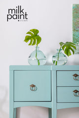 Two glass vases with green leaves on a blue cabinet painted in Fusion Mineral Paint Sea Glass.
