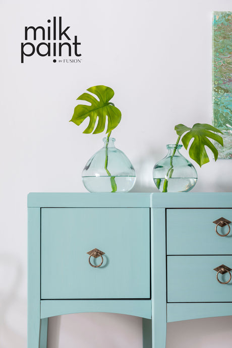 Two glass vases with green leaves on a blue cabinet painted in Fusion Mineral Paint Sea Glass.