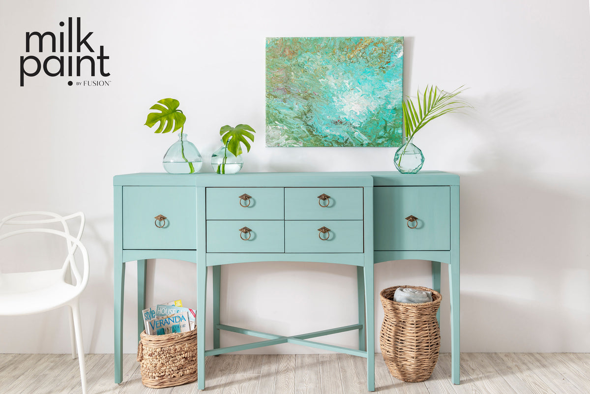 Sideboard in Fusion Mineral Paint Sea Glass with drawers, baskets, glass vases, and an abstract green painting above.