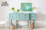Sideboard in Fusion Mineral Paint Sea Glass with drawers, baskets, glass vases, and an abstract green painting above.
