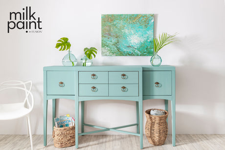 Sideboard in Fusion Mineral Paint Sea Glass with drawers, baskets, glass vases, and an abstract green painting above.