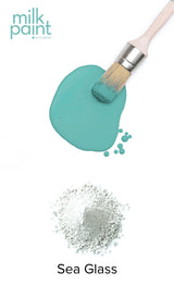 Fusion Mineral Paint brush resting on spilled Sea Glass paint atop white powder labeled Sea Glass.