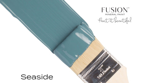 Paintbrush with Seaside Fusion Mineral Paint label and coastal blue bristles on a white background.