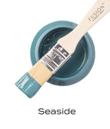 Open Seaside Fusion Mineral Paint jar with brush resting on top, bristles coated in coastal blue paint.