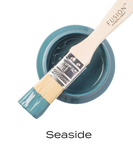 Open Seaside Fusion Mineral Paint jar with brush resting on top, bristles coated in coastal blue paint.