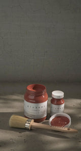 Three jars of Fusion Mineral Paint Sienna Alchemy, a paintbrush, and a lid arranged on a gray surface.