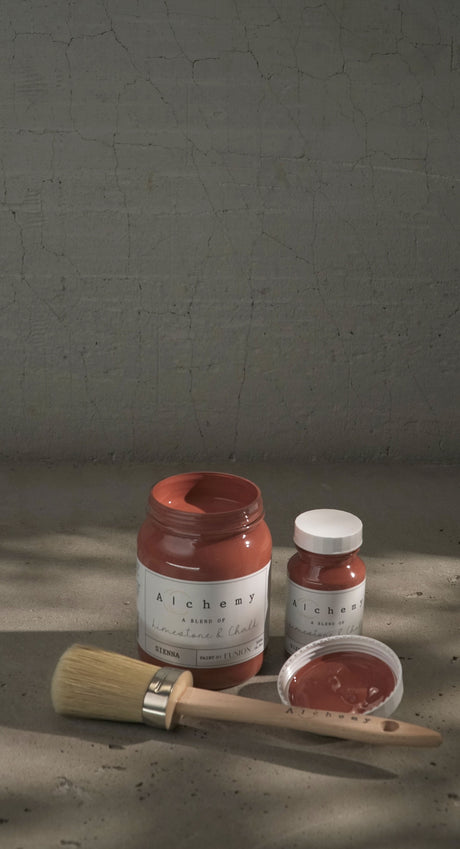 Three jars of Fusion Mineral Paint Sienna Alchemy, a paintbrush, and a lid arranged on a gray surface.
