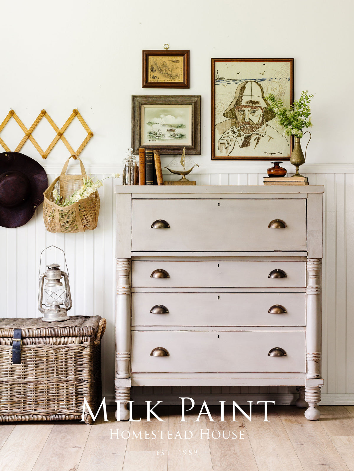 White dresser in Homestead House Silhouette Milk Paint with brass handles, next to a wicker trunk.