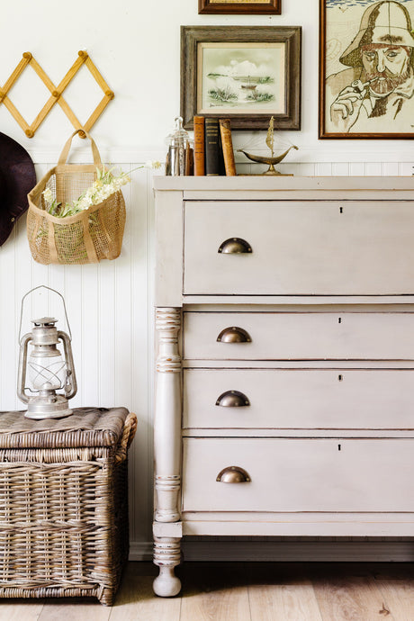 Wicker basket, lantern, and dresser painted in Homestead House Silhouette Milk Paint with books and wall art.