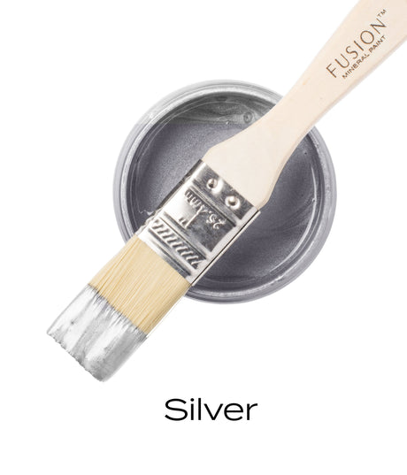 Paintbrush resting on a Silver Metallic Fusion Mineral Paint container, top-down view.