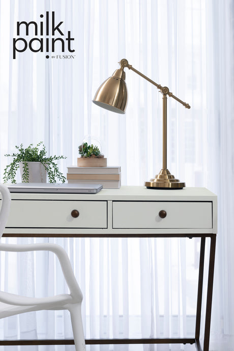White desk with two drawers, brass lamp, books, and Fusion Silver Screen Paint accents.