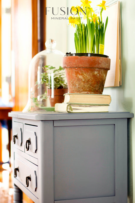 Gray cabinet painted with Soap Stone Fusion Mineral Paint, shown with daffodils, books, and a terrarium on top.