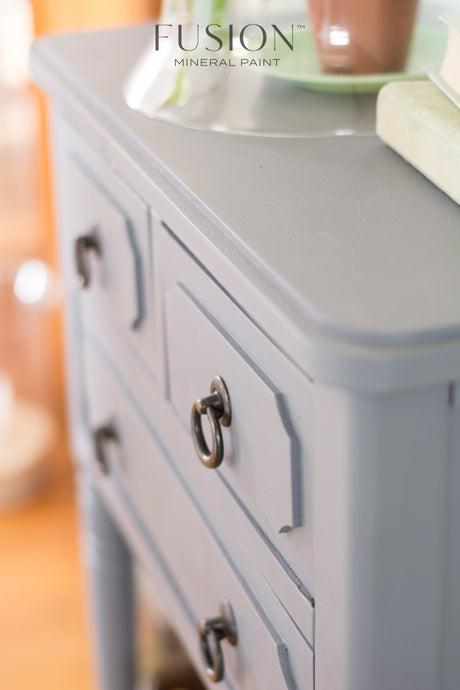 Dresser in Soap Stone by Fusion Mineral Paint with black handles, books, and a plant on top.