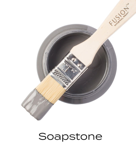 Open jar of Fusion Mineral Paint in Soap Stone, deep gray, with brush dipped in paint.