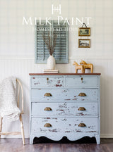 Dresser in Solstice Blue Milk Paint by Homestead House with brass handles, shown next to a cream chair.