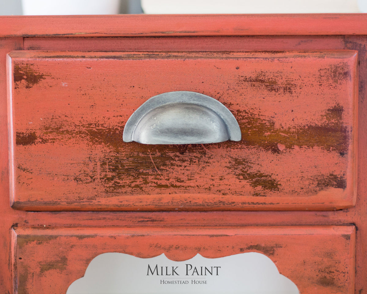 Distressed red wooden drawer painted with Spice Milk Paint by Homestead House, brand text below.