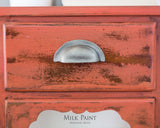 Distressed red wooden drawer painted with Spice Milk Paint by Homestead House, brand text below.