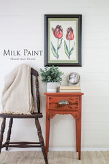 Wood chair next to red side table with plant, clock, tulip art, and Homestead House Spice Milk Paint on white wall.