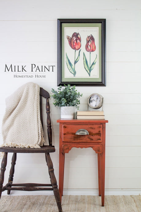 Wood chair next to red side table with plant, clock, tulip art, and Homestead House Spice Milk Paint on white wall.