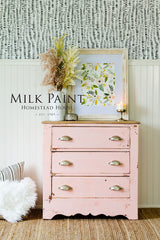 Pink distressed dresser in Homestead House Spring Blossom Milk Paint with floral art, dried flowers, and candle on top.