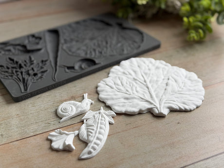 Spring Garden Mould by IOD featuring leaf, snail, flower, and pea pod designs arranged on wood.