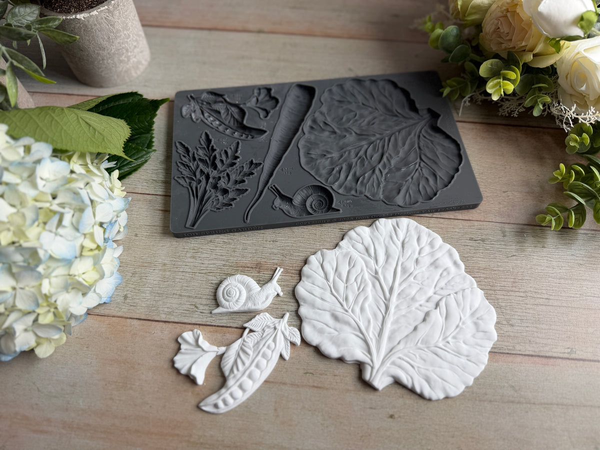 Gray cabbage leaf and white clay casts from Spring Garden Mould by IOD displayed on a wooden surface.