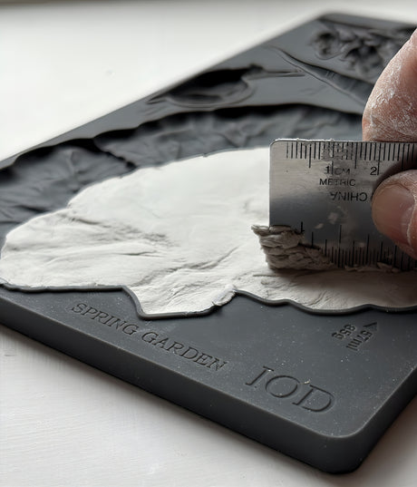 Hand spreading plaster with a metal ruler in a Spring Garden Mould by I.O.D. on a white surface.
