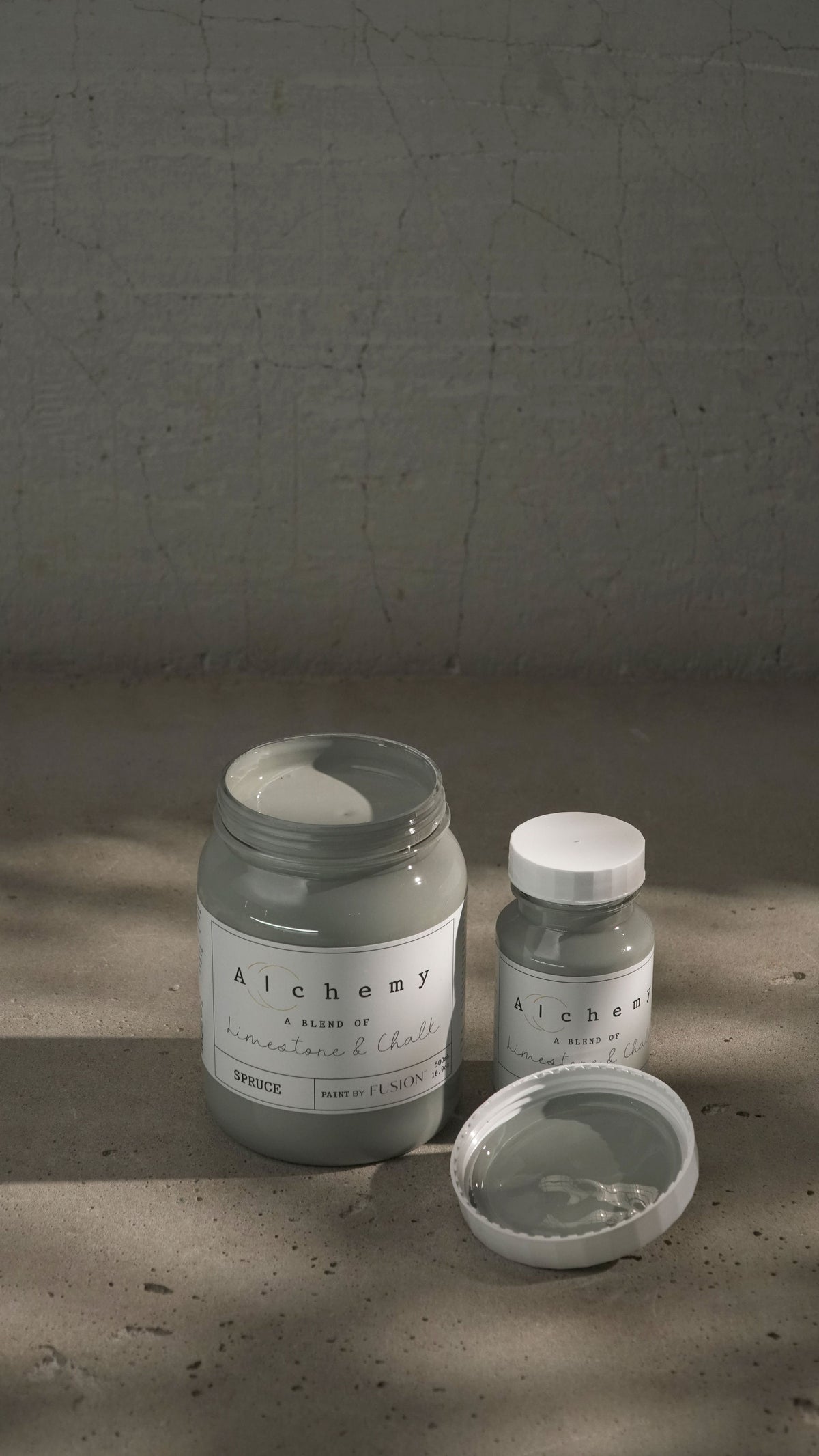 Two jars of Spruce Alchemy Paint by Fusion Mineral Paint, one opened, displayed side by side on a textured surface.