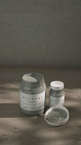 Two jars of Spruce Alchemy Paint by Fusion Mineral Paint, one opened, displayed side by side on a textured surface.
