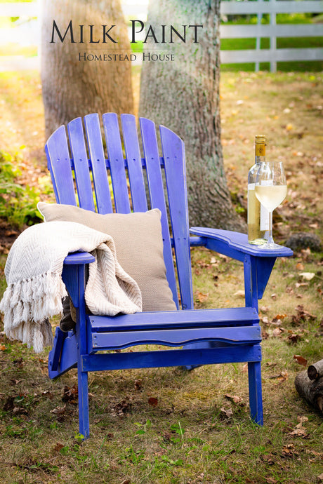 Blue wooden chair painted with Homestead House St-Laurent Blue, with beige pillow, blanket, and a glass of white wine.
