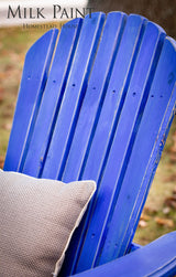 Wooden Adirondack chair painted Homestead House St-Laurent Blue Milk Paint, shown outdoors on grass with leaves.
