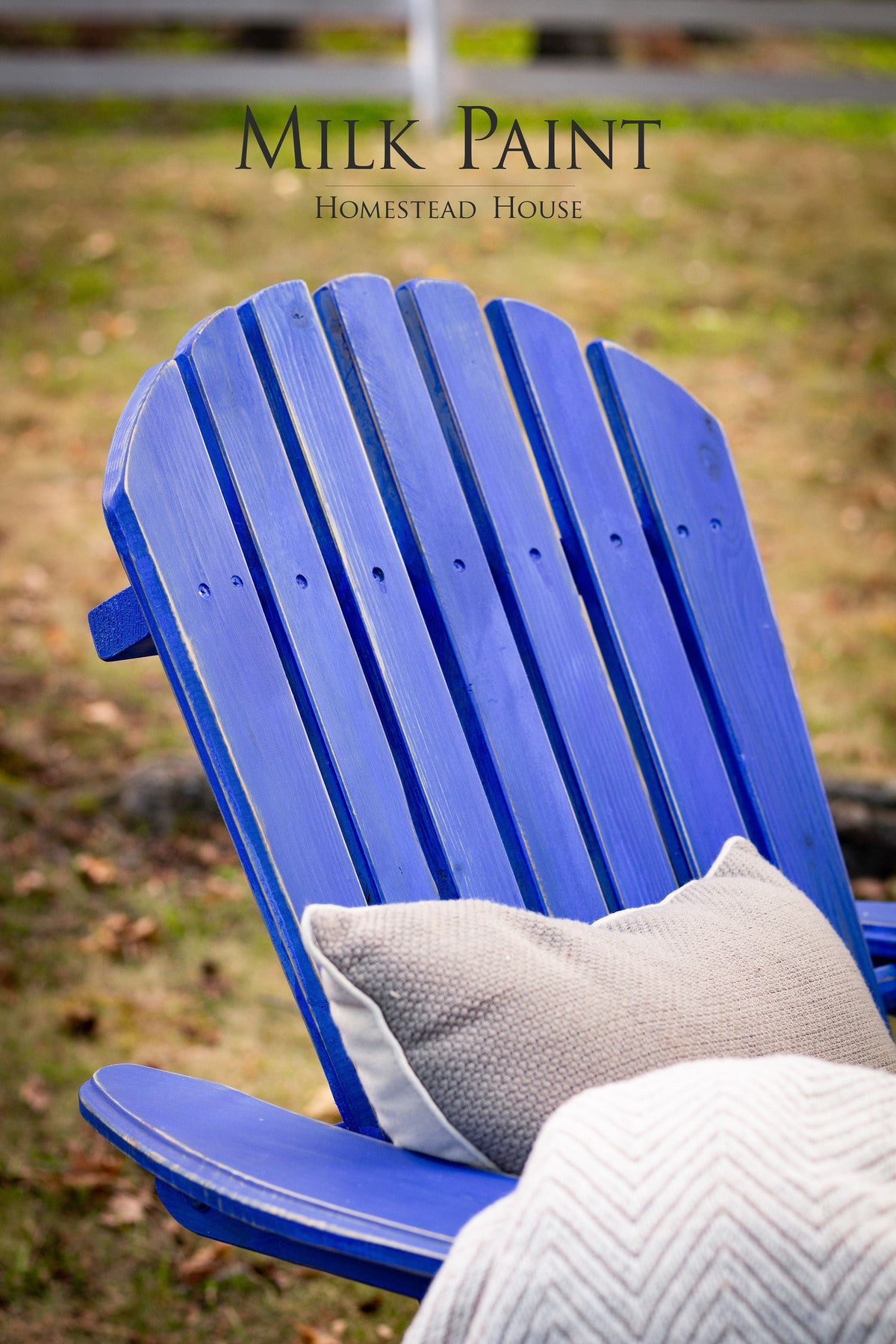 Adirondack chair in St-Laurent Blue Milk Paint by Homestead House with beige pillow and blanket.