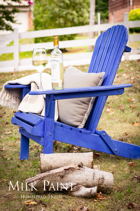 Blue Adirondack chair in St-Laurent Blue Milk Paint by Homestead House with a wine bottle and glass on the seat.