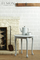 Small round table with teapot and cup beside a white brick wall in Sterling Fusion Mineral Paint matte finish.