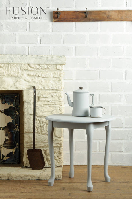 Small round table with teapot and cup beside a white brick wall in Sterling Fusion Mineral Paint matte finish.