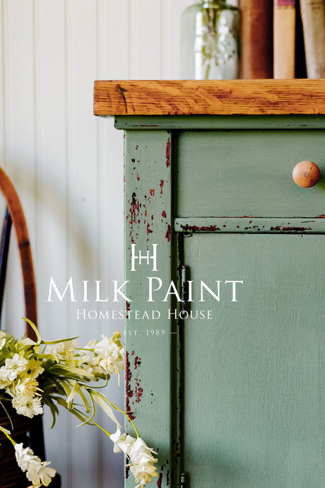 Stockholm Green Milk Paint cabinet by Homestead House with wood top, single knob, stacked books, and flowers.