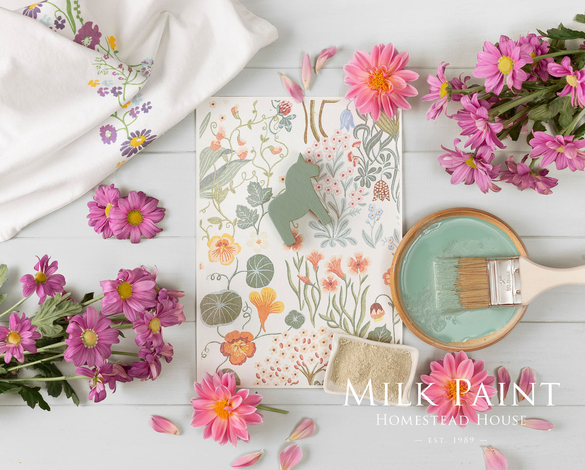 Stockholm Green Milk Paint by Homestead House with floral card, paintbrush, and pink flowers on white table.