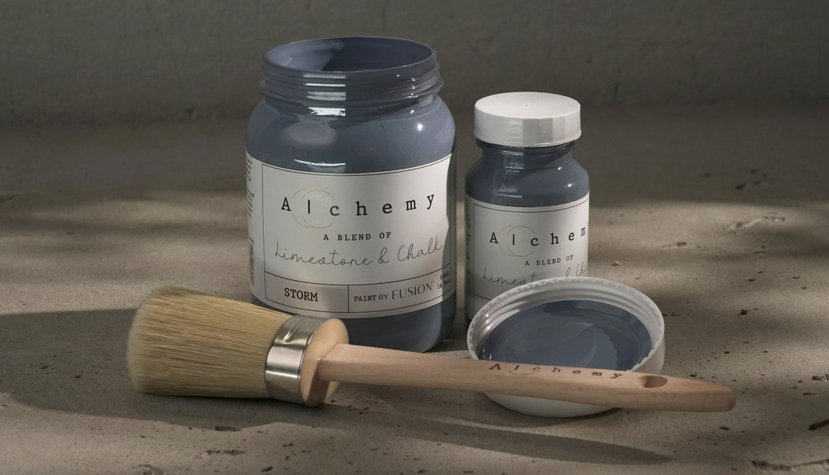 Two jars of Fusion Mineral Paint in Storm Alchemy with a brush on a gray surface.