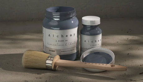 Two jars of Fusion Mineral Paint in Storm Alchemy with a brush on a gray surface.