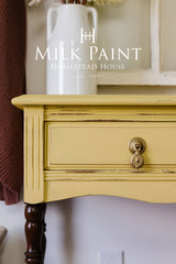 Yellow Swedish Yellow Milk Paint drawer by Homestead House, brass handle, wood legs, white vase on top.