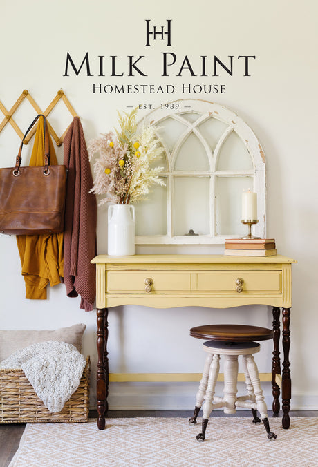 Homestead House Swedish Yellow Milk Paint desk beneath Homestead House sign, with vase, mirror, and candle on top.