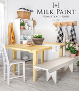 Dining table in Homestead House’s Swedish Yellow Milk Paint with white bench and plants nearby.