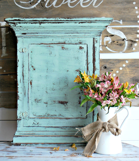 Distressed teal cabinet painted with Old Fashioned Milk Paint Sweetie Jane next to a burlap-tied floral pitcher.