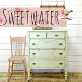 Pink chair and pale green dresser in Old Fashioned Milk Paint beside a Sweetwater sign on white shiplap wall.