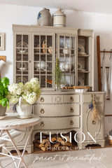 Beige vintage hutch painted in Tapestry by Fusion Mineral Paint, with dishes, decor, and firewood stored below.