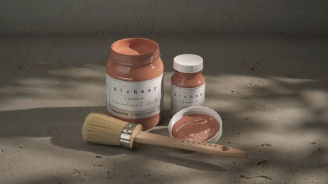 Paintbrush with open Terracotta Alchemy Paint by Fusion jar on a gray surface. Brand: Fusion Mineral Paint.