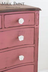 Distressed dresser in Texas Rose Milk Paint with three white flower knobs and visible wood grain.