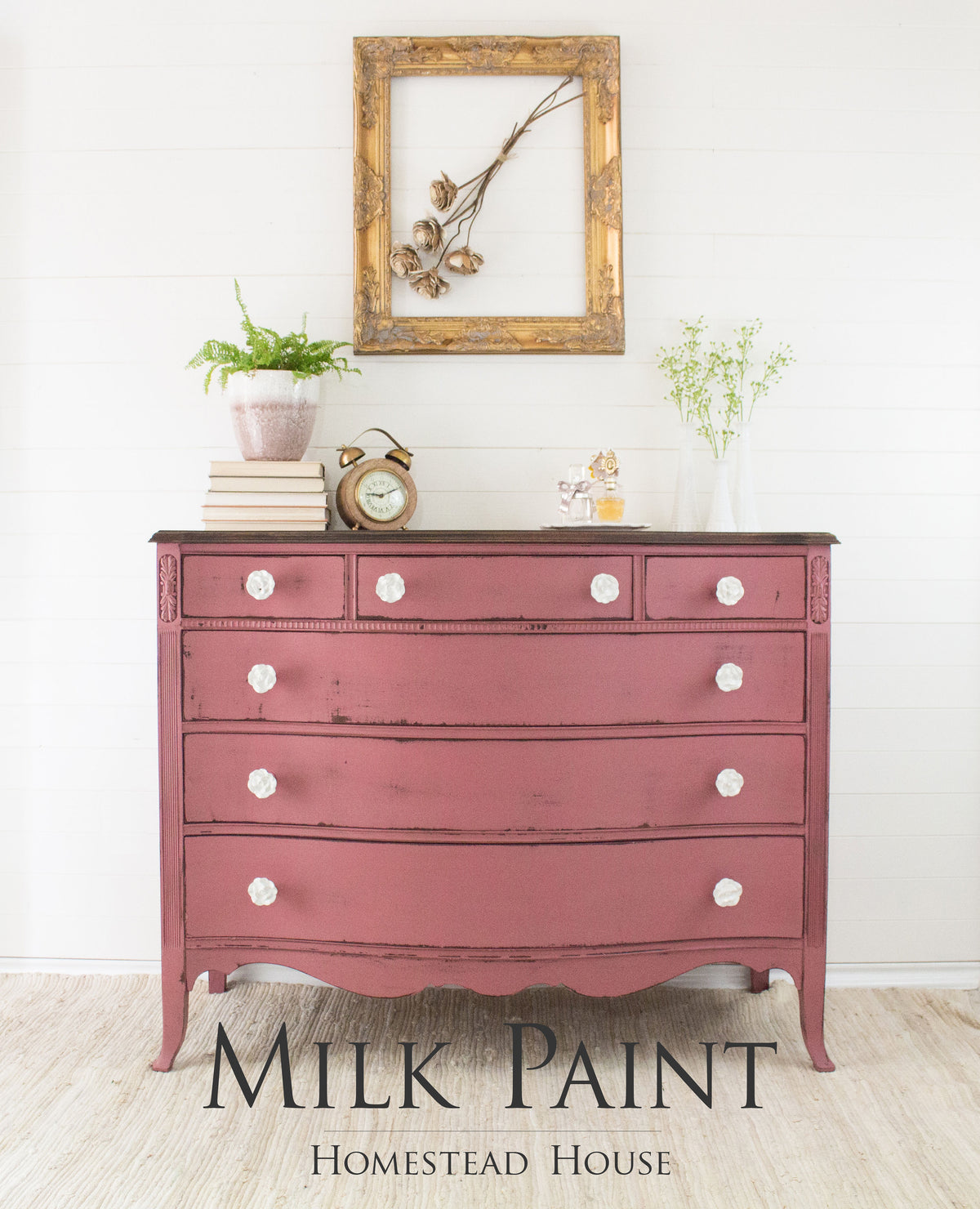 Dresser painted in Homestead House Texas Rose Milk Paint with plants, a clock, and framed art displayed on top.