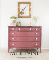 Dresser painted in Homestead House Texas Rose Milk Paint with plants, a clock, and framed art displayed on top.